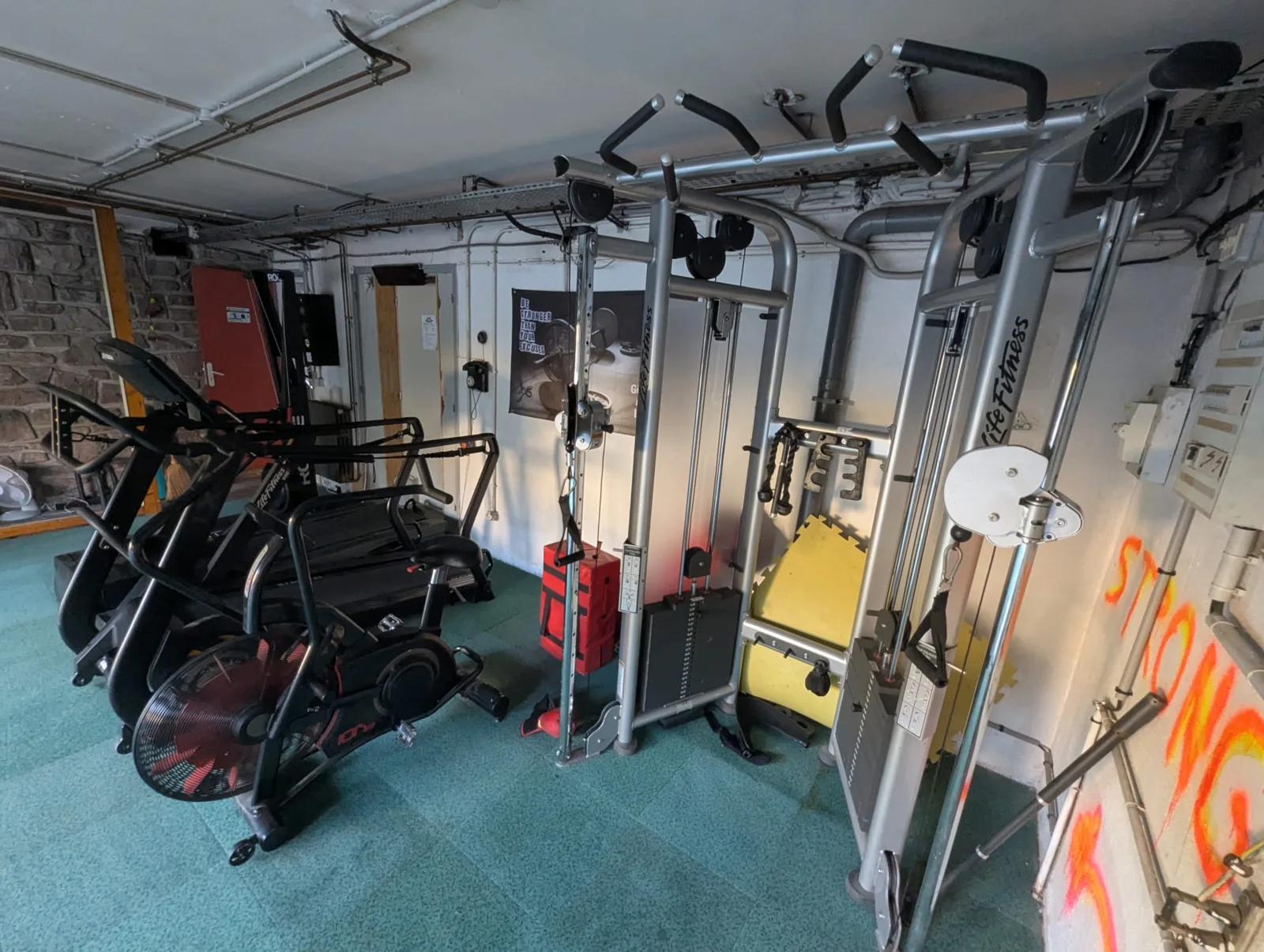 Cardio (air bike, tapis) et station à poulies Life Fitness.